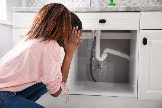 Woman panicked looking under sink at busted pipe